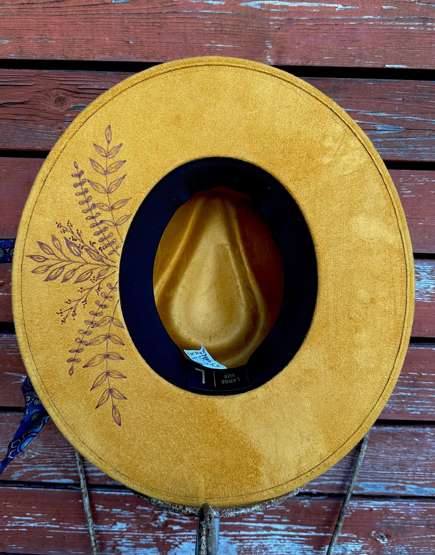 Yellow faux suede hat with Handburned wild-flowers on under brim on a wooden surface