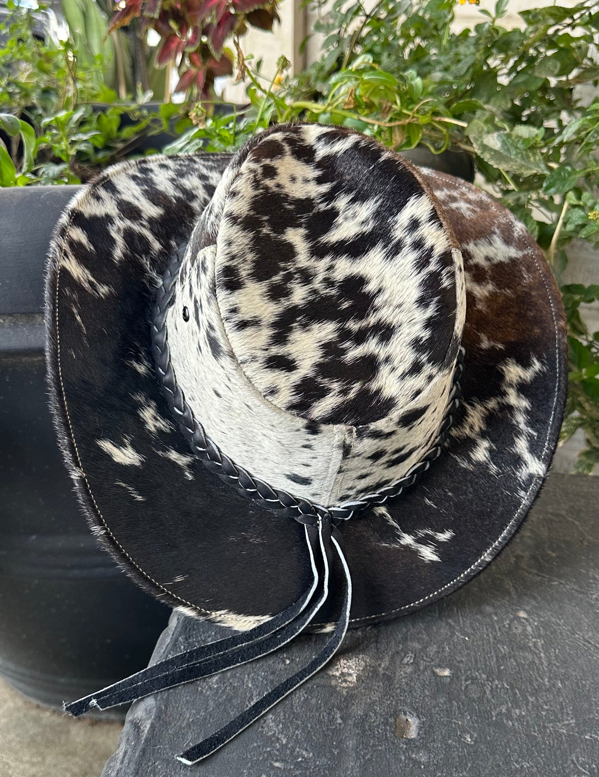 Goat hide Cowboy hat with black and white pattern on a stone surface with plants in the background