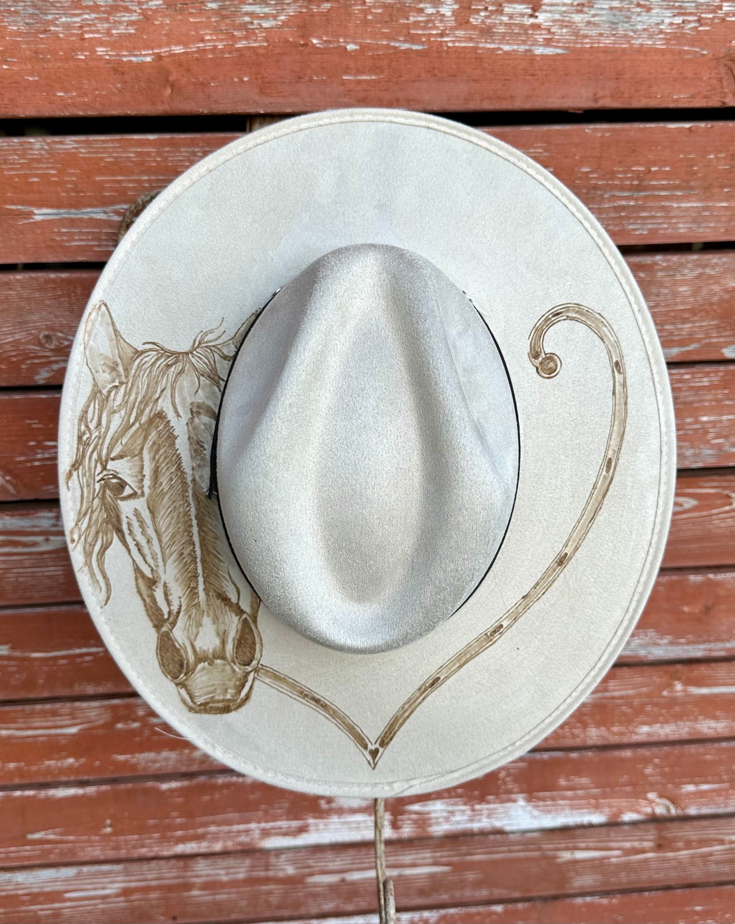 White cowboy hat with horse design on a wooden surface