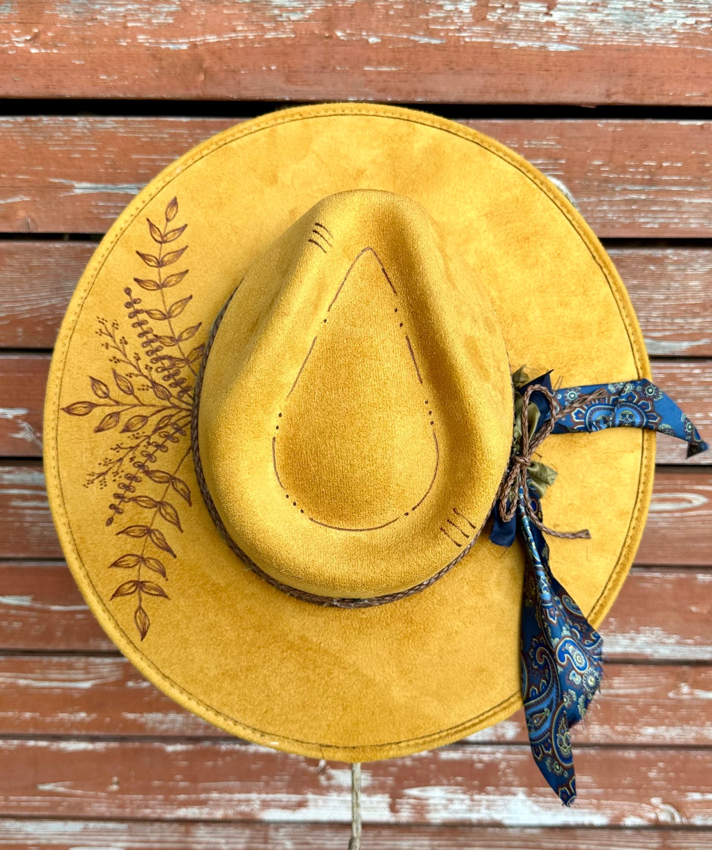 Yellow faux suede cowboy hat with Handburned wildflowers on a wooden surface
